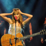 CONFESSION In Taylor Swift Massacre Plot Taylor Swift holding guitar on stage, background singers behind.