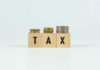 Bezos Drops Tax Bombshell: Pay Zero Plan! Blocks spelling 'TAX' with coins stacked beside them