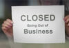 CENTURY-OLD Site SHUTDOWN – Employees Shattered! A person holding a sign that reads 'CLOSED Going Out of Business'