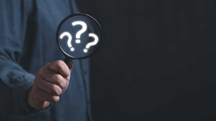 Hand holding magnifying glass with question marks.