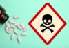 A bottle of pills spilled next to a poison warning sign