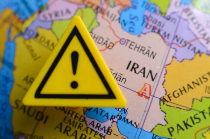 Close,Up,View,Of,Of,Iran,Country,At,The,Map A yellow warning sign placed on a map highlighting Iran