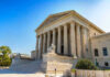 Stone building with columns and statues, clear blue sky.