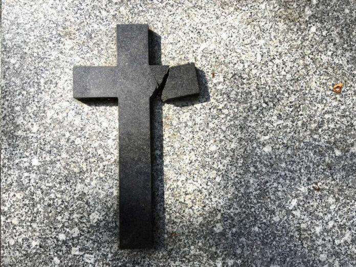 shutterstock_1119238859 Broken black cross on a gray surface.