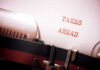War Tax Hits American Homes Hard A typewriter with a paper displaying the words 'TAXES AHEAD'