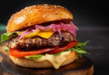 Burger Chain’s Grass-Fed Gamble Close-up of a gourmet cheeseburger with lettuce, tomato, and pickled onions