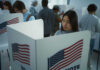 People voting in booths with American flags.
