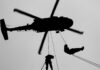 Silhouette of a helicopter with two individuals being lowered by ropes