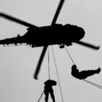Silhouette of a helicopter with two individuals being lowered by ropes