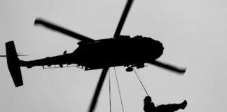Silhouette of a helicopter with two individuals being lowered by ropes