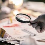 GPS Bombshell Upends Lynette Hooker Investigation Gloved hand holding a magnifying glass over scattered forensic documents