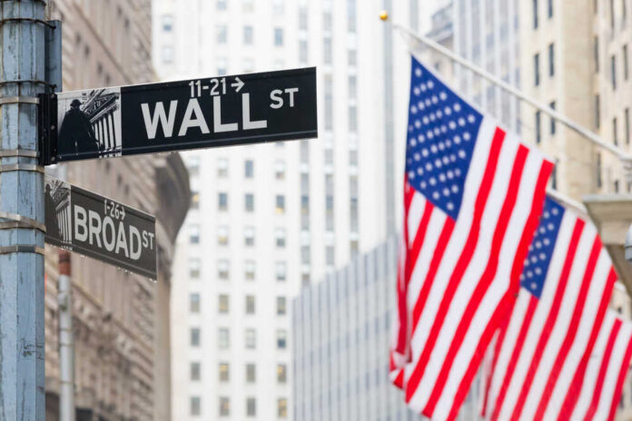Wall,Street,Sign,In,New,York,With,American,Flags,And Street signs for Wall Street and Broad Street with American flags