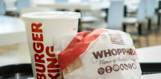 A Whopper Jr. burger wrapped in paper next to a Burger King drink