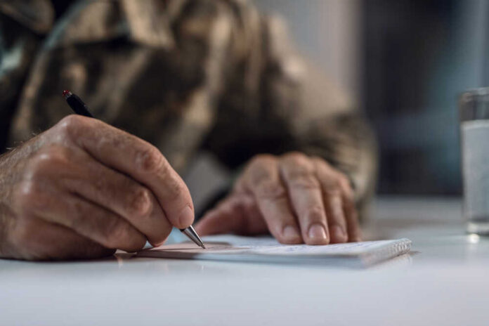 Close,Up,Of,Mature,Army,Soldier,Writing,A,Letter. A hand writing on a notepad with a pen
