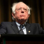 Bernie Sanders Demands Half?! Bernie Sanders in suit speaking at podium.