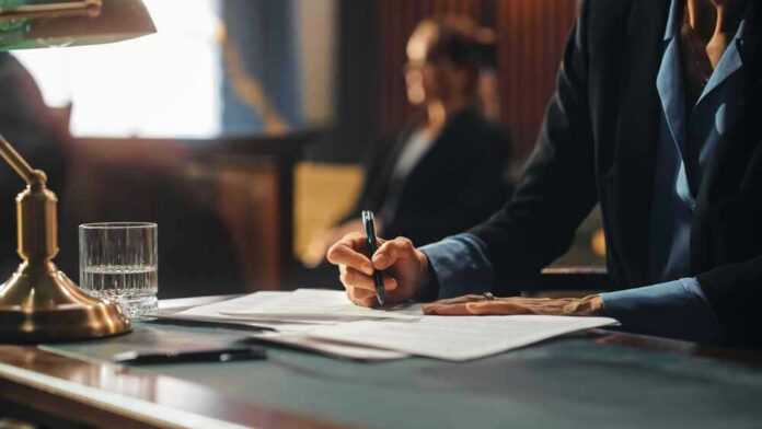 shutterstock_2056444919 Person writing at desk with documents and glass.