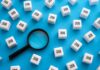 Vanishing Workers Skew ‘Good’ Jobs Report Magnifying glass among cubes labeled job on blue background