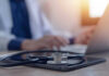 Hero Pilot’s Diagnosis Sparks Outpouring Of Support Stethoscope and tablet on desk, doctor using laptop.