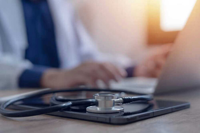 shutterstock_2468694473 Stethoscope and tablet on desk, doctor using laptop.
