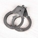 A pair of metallic handcuffs resting on a light wooden surface