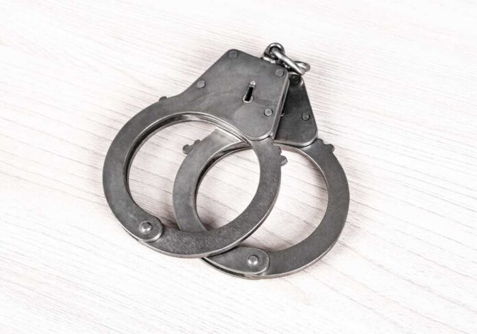 Closed,Handcuffs,On,The,Wooden,Table,Closeup A pair of metallic handcuffs resting on a light wooden surface