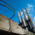 America’s Missiles Nearly GONE?! Missiles silhouetted against American flag background with sunset.