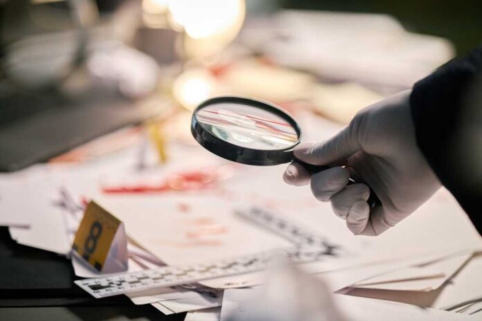 Gloved,Hand,Holding,Magnifying,Glass,Examining,Documents,On,Cluttered,Workspace Gloved hand holding a magnifying glass over scattered forensic documents