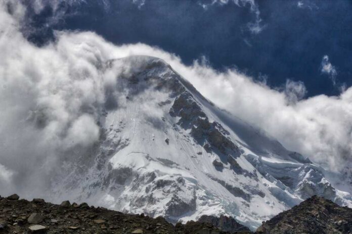 A,Beautiful,View,Of,A,Strong,Avalanche,Coming,Down,The Snow-covered mountain peak partially obscured by clouds