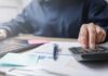 Housing Squeeze Forces Record Boomerang Kids Person using a calculator while working on a laptop and reviewing documents