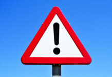 VIDEO: Gold Pit Collapse — Death Toll Climbing A triangular warning sign with an exclamation mark against a blue sky