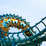 Roller coaster train twists through a teal and yellow loop