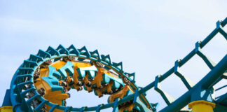 Roller coaster train twists through a teal and yellow loop