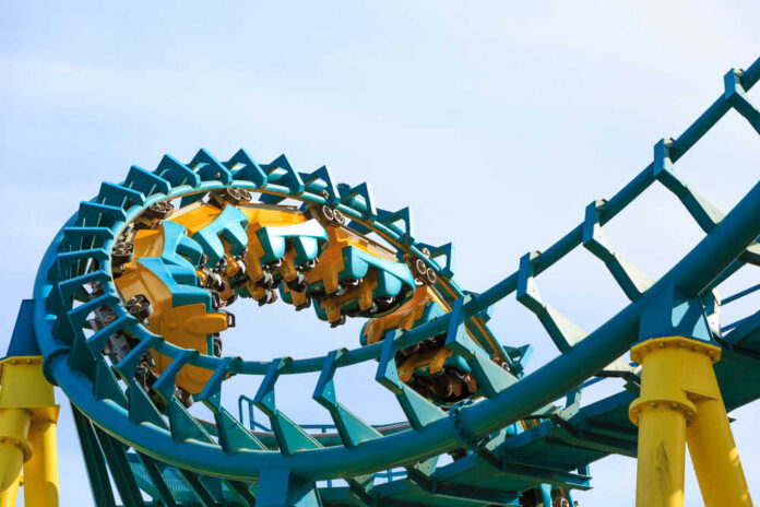 Roller coaster train twists through a teal and yellow loop