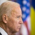 Biden Pardon Twist Jolts Fauci Fight Joe Biden, side profile, flags behind.