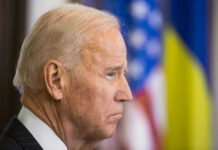 Biden Pardon Twist Jolts Fauci Fight Joe Biden, side profile, flags behind.