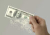Two Trillion Timebomb Ticks Hand holding a disintegrating hundred dollar bill.