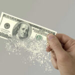 Two Trillion Timebomb Ticks Hand holding a disintegrating hundred dollar bill.