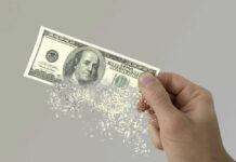 Two Trillion Timebomb Ticks Hand holding a disintegrating hundred dollar bill.