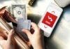 Credit Cards Climb, Everything Else Falls Person holding a credit card and cash while looking at a phone displaying debt information
