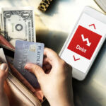 Credit Cards Climb, Everything Else Falls Person holding a credit card and cash while looking at a phone displaying debt information