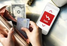 Person holding a credit card and cash while looking at a phone displaying debt information