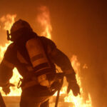 Inferno Swallows Spokane — 60,000 Flee Firefighter in full gear entering a burning building staircase