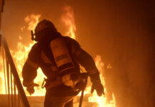 Inferno Swallows Spokane — 60,000 Flee Firefighter in full gear entering a burning building staircase