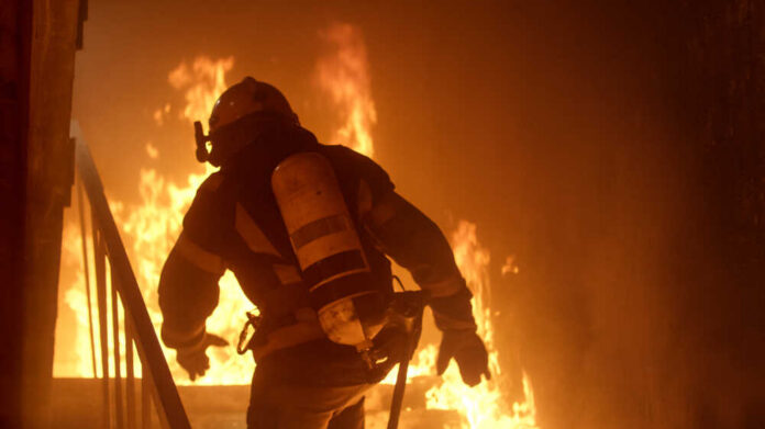 Brave,Firefighter,Runs,Up,The,Stairs.,Raging,Fire,Is,Seen Firefighter in full gear entering a burning building staircase