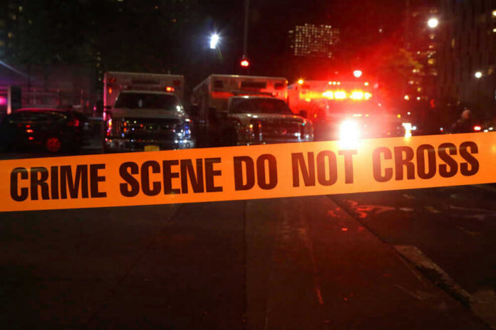 shutterstock_746018290 Crime scene tape with emergency vehicles in background.
