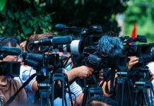 TV news cameras crowding together at an outdoor event