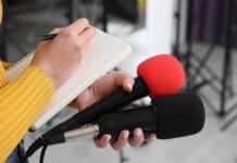 Journalist holding two microphones while writing in a notebook