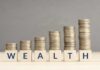 Stacks of coins arranged next to wooden blocks spelling 'WEALTH'