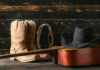 Cowboy boots, hat, and guitar on wooden surface.