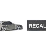 Recall Panic: Fuel Tanks Can Drop A miniature gray sports car next to a black sign that reads 'RECALL'